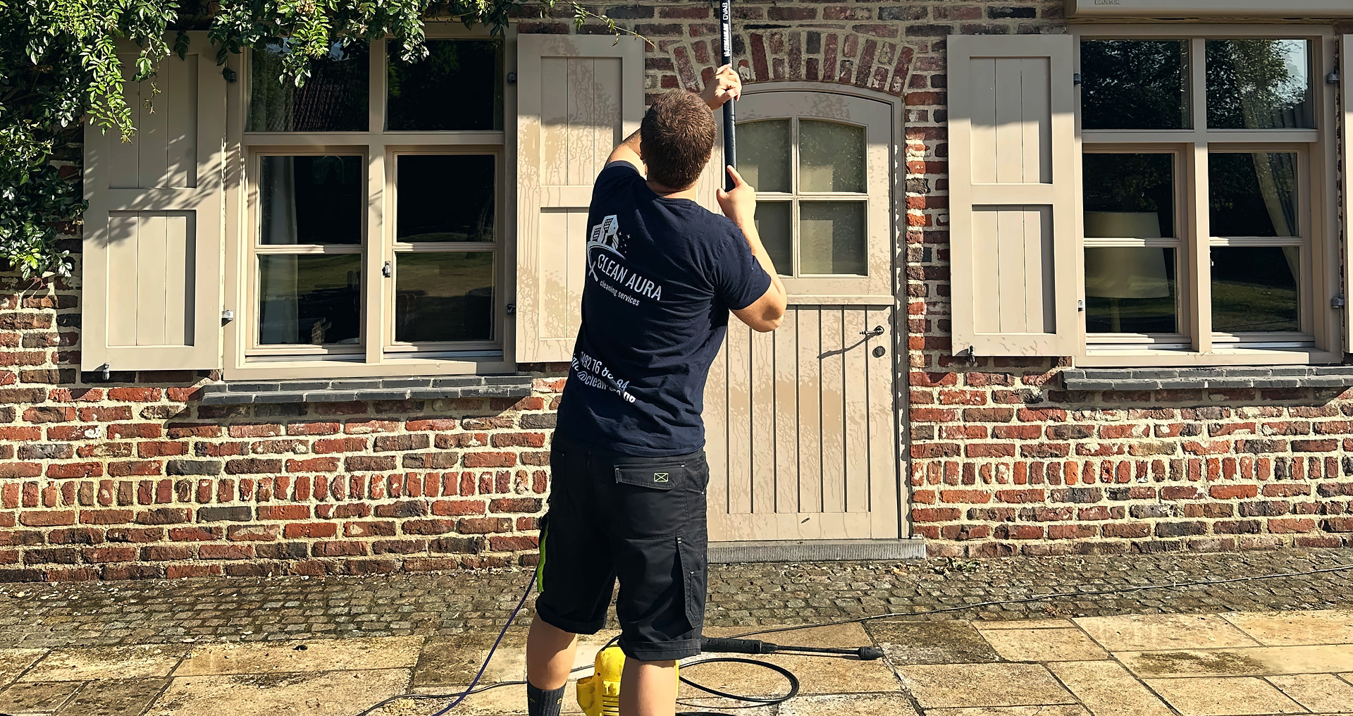 Clean Aura medewerker wast met een telescoopsteel de ramen van een bakstenen woning
