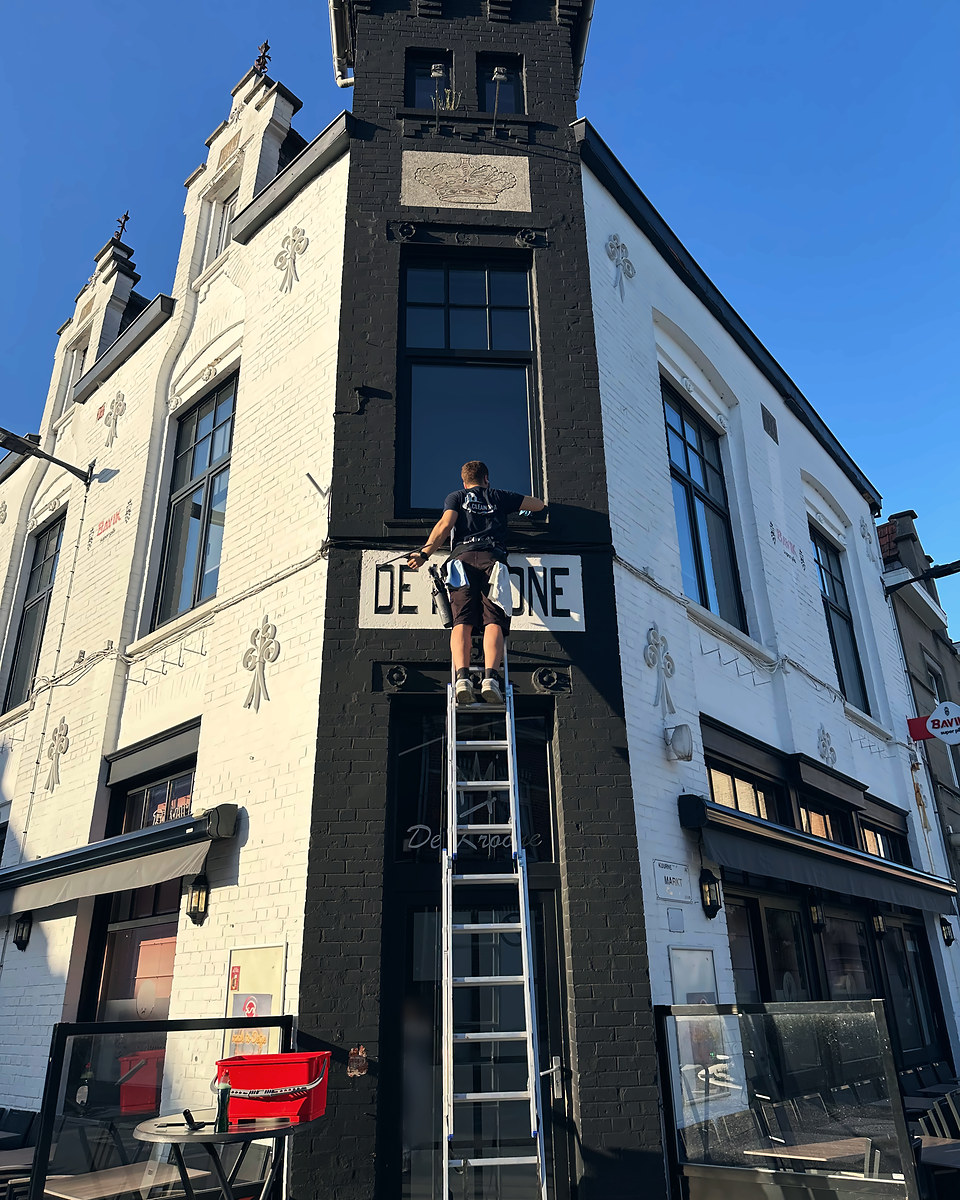 Clean Aura medewerker wast op een ladder de ramen van een café op de hoek van de markt