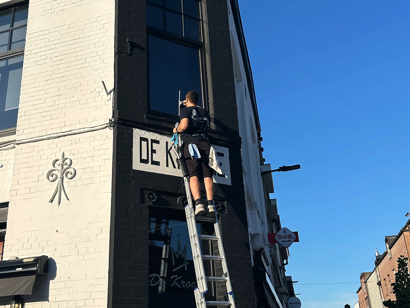 Clean Aura medewerker wast op een ladder de ramen van een café, boven het uithangbord