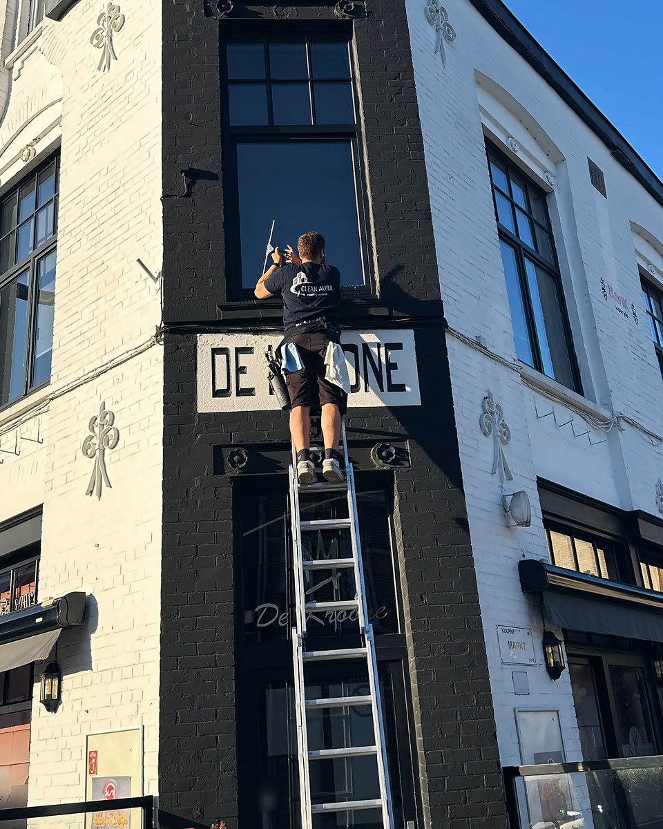 Clean Aura medewerker wast vanop een ladder een hoog raam boven het uithangbord van een café