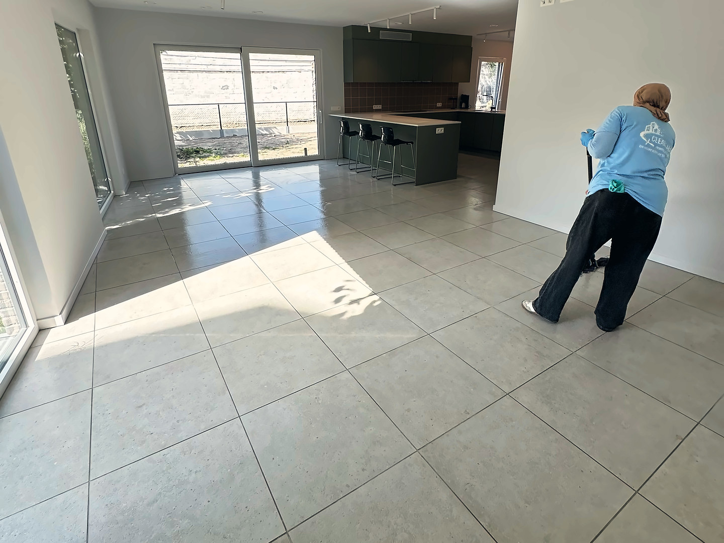 Clean Aura medewerkster dweilt de tegelvloer van een lichte, lege woning