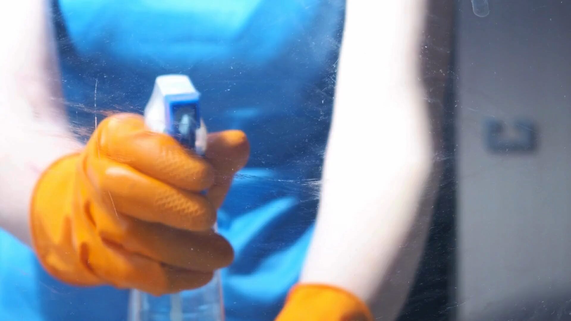 Clean Aura medewerker reinigt een ruit met sproeiflacon, gezien door het glas